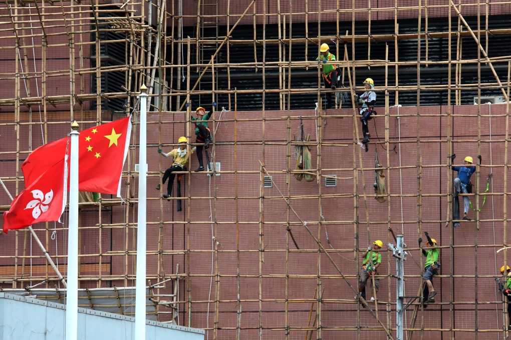 Construction workers remove the scaffolding on a building in Sham Shui Po as the Hong Kong and Chinese flags flutter in the foreground, in June 2019. Photo: Felix Wong