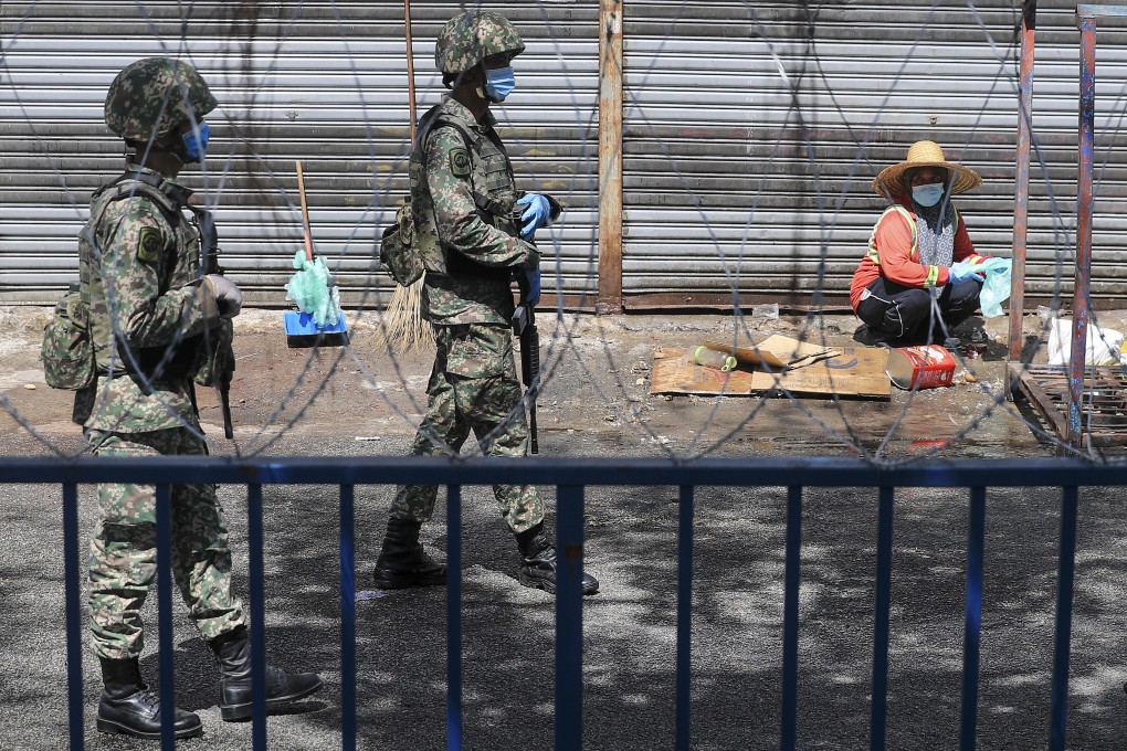 A worker looks on as members of Malaysia’s armed forces patrol an area under lockdown in Kuala Lumpur on Tuesday. Photo: EPA