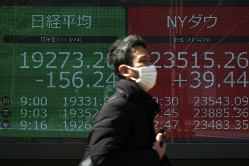 A man wearing a mask to help stop the spread of the new coronavirus walks past an electronic stock board showing Japan's Nikkei 225 and New York Dow indexes at a securities firm in Tokyo on April 24, 2020. Photo: Associated Press