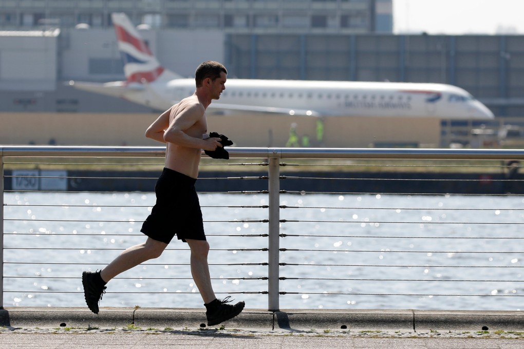 A jogger exercises at Gallions Point Marina with a British Airways plane parked at London City Airport in the background. Photo: AFP