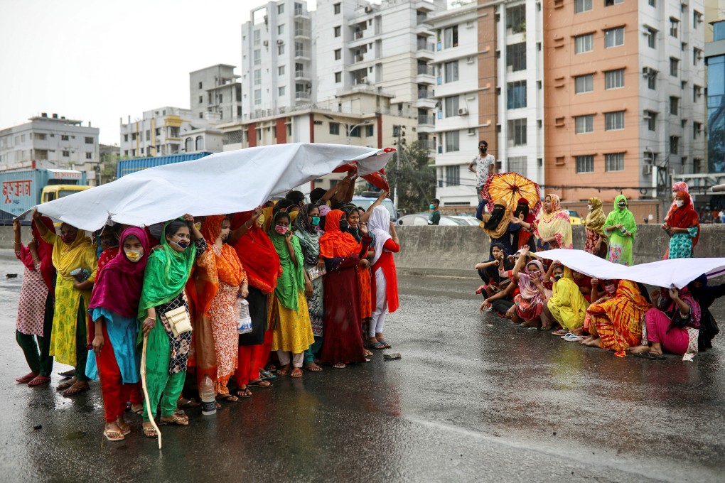 Bangladeshi garment workers shelter from the rain under a banner as they protest to demand their due wages, during a coronavirus lockdown in Dhaka on April 15. Photo: Reuters