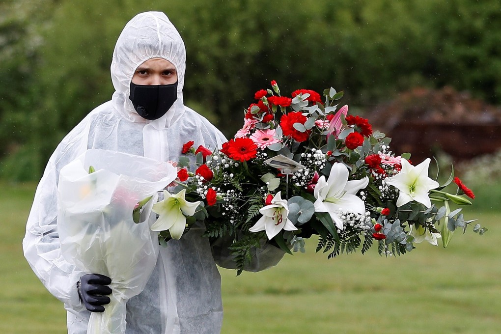 A funeral service worker in protective gear carries flowers at a cemetery in London in April. Photo: Reuters