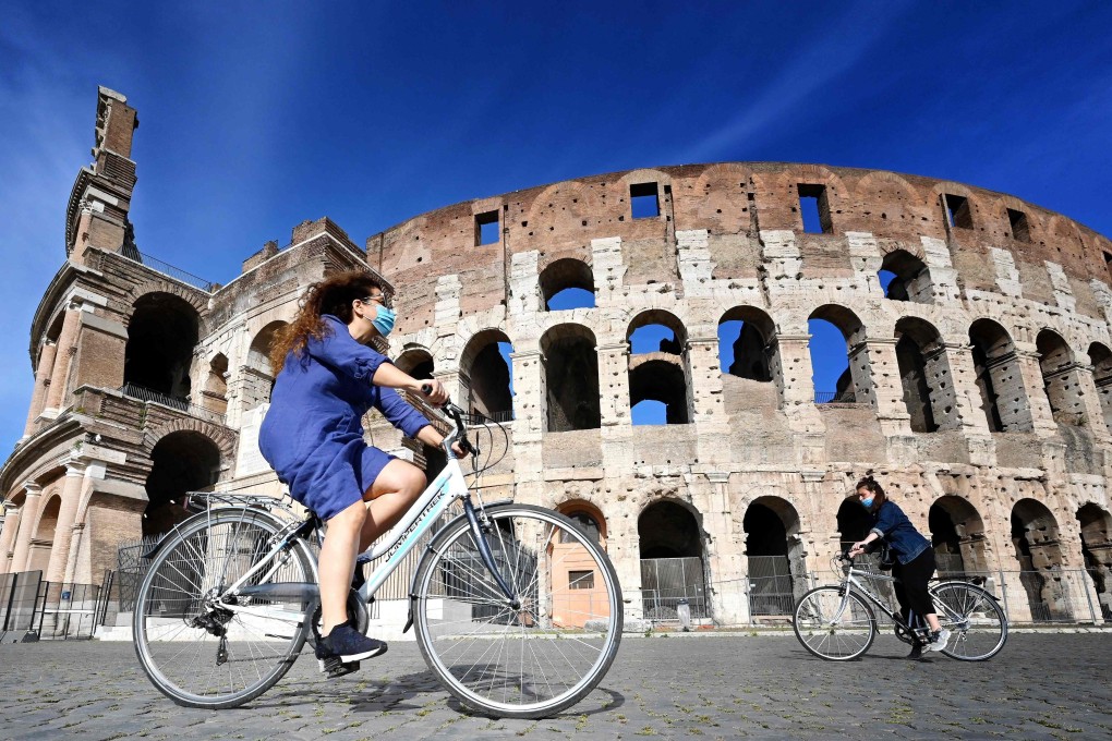 Women ride a bicycle past the Colosseum monument in Rome. Photo: AFP