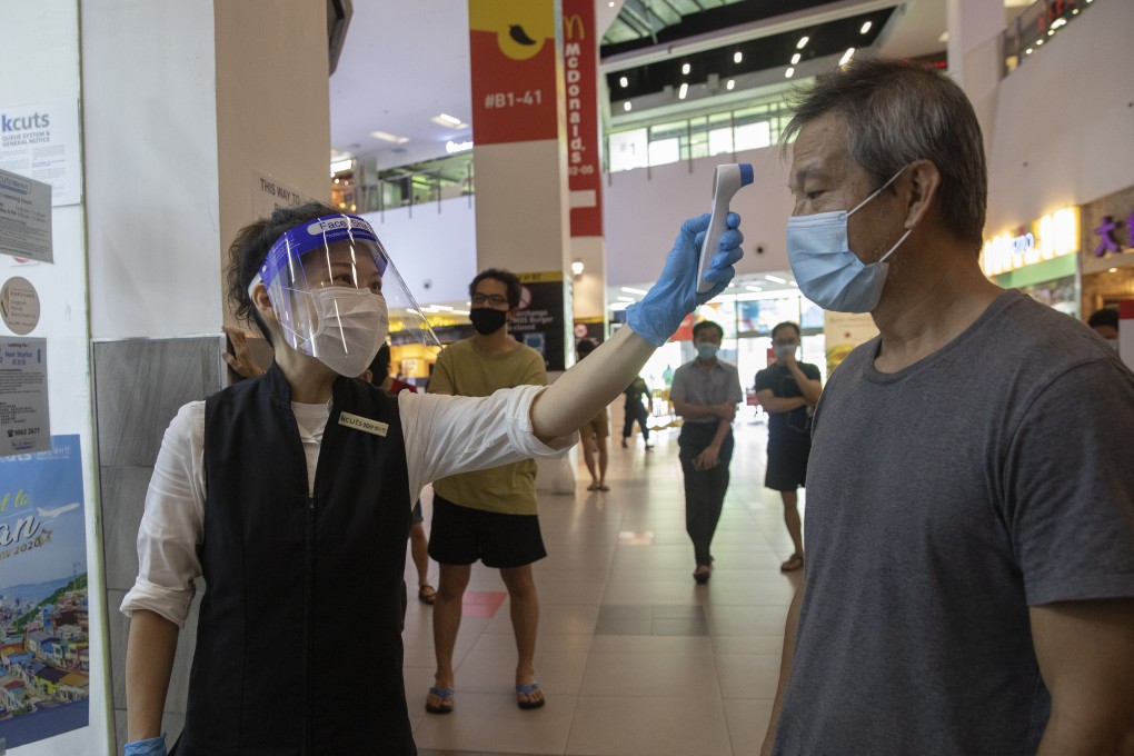 A hairdresser wearing a protective mask and a face shield checks the temperature of customers at a hair salon in Singapore. Photo: EPA