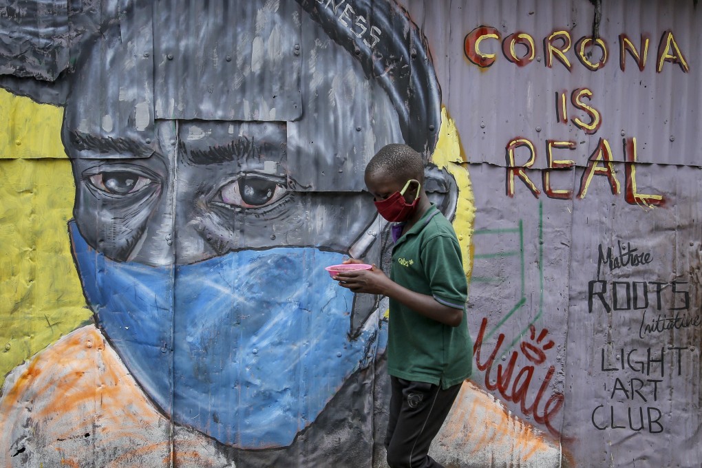 A boy wearing a mask carries a bowl of githeri, a meal of beans and maize, as he walks past a mural warning of the coronavirus in Mathare, a cluster of slums in Nairobi, Kenya. Photo: AP