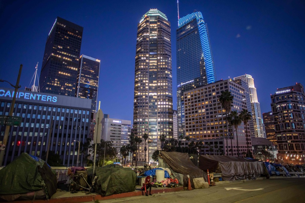 A homeless woman sits on the sidewalk by a row of tents as she checks her cellphone in downtown Los Angeles. Photo: AFP
