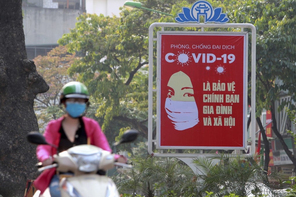 A motorcyclist drives past a Covid-19 poster in Hanoi. Photo: AP