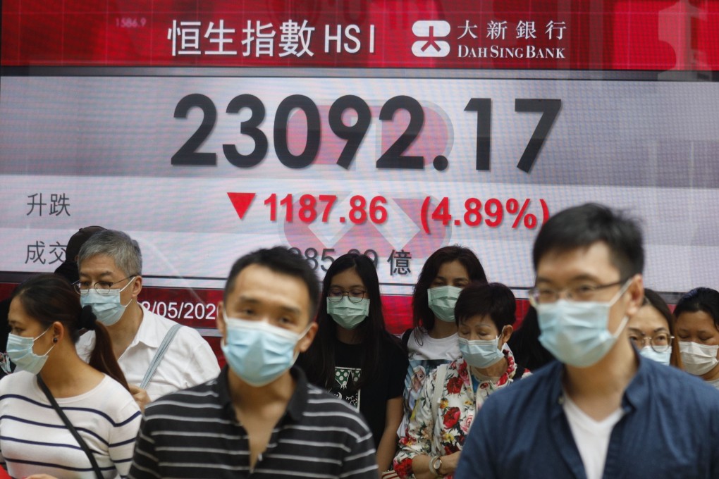 People wearing face masks walk past an electronic board showing the Hong Kong share index on May 22. Photo: AP