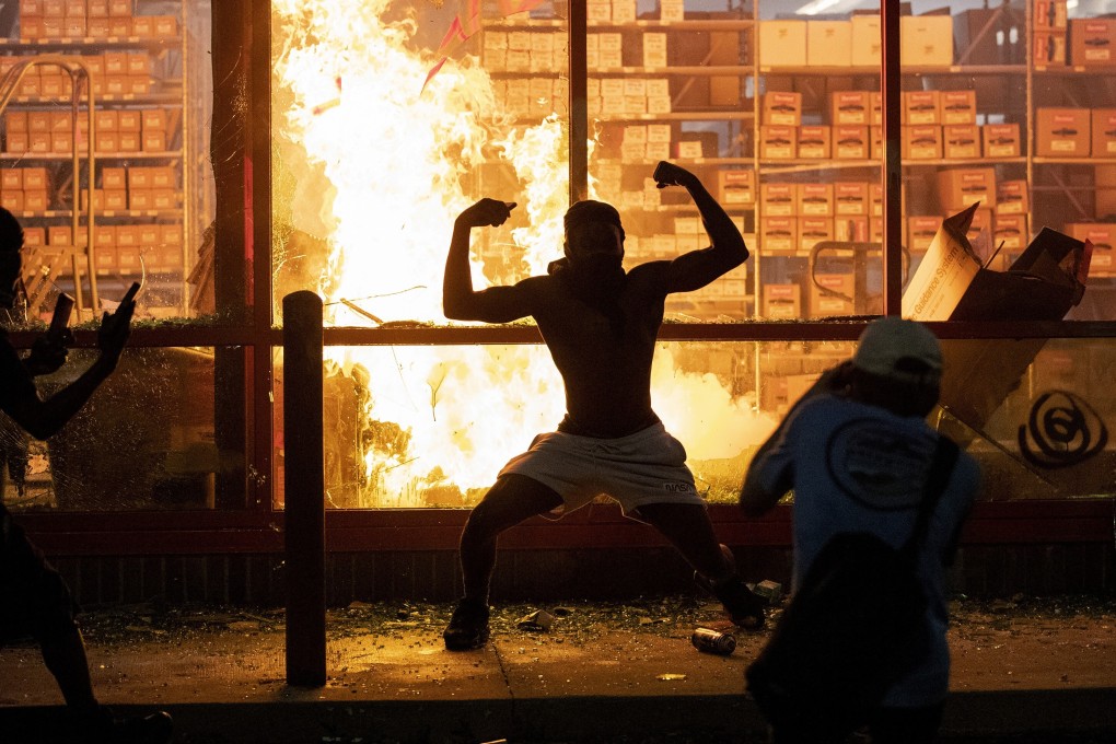 A man poses for photos in front of a fire at an AutoZone store, while protesters hold a rally for George Floyd in Minneapolis. Photo: AP