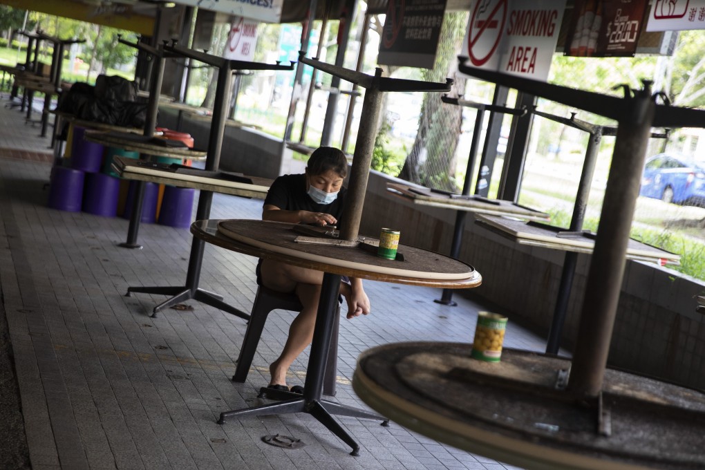 A woman wearing a protective face mask sits in an empty Singapore coffee shop where tables have been packed up to prevent people sitting down during the 'circuit breaker' partial lockdown. Photo: EPA