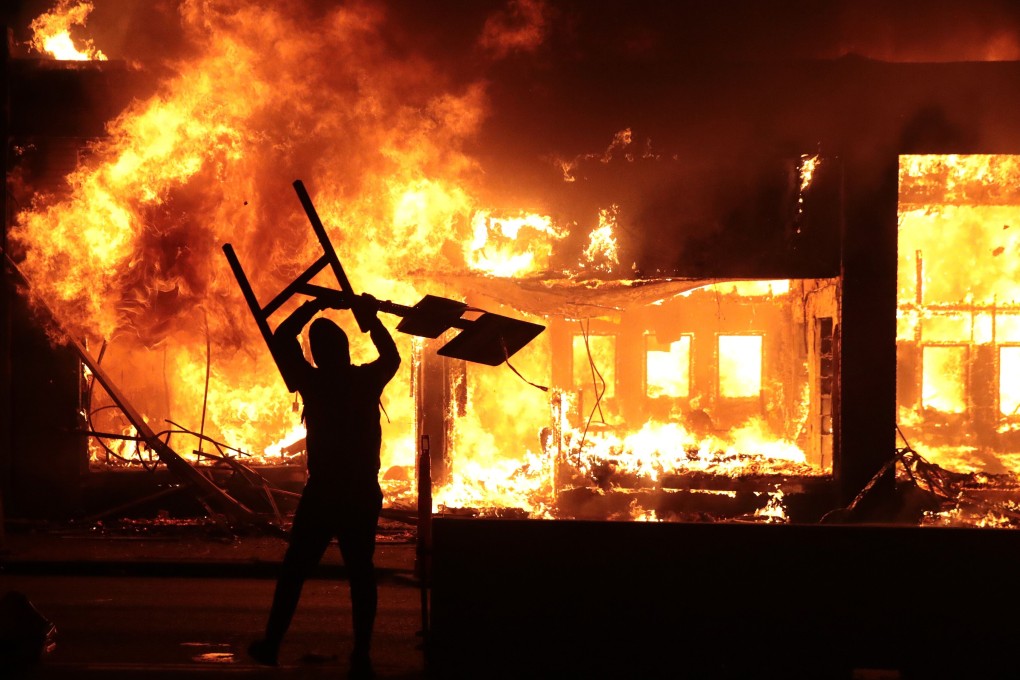 A man holds up a sign near a burning building during protests sparked by the death of George Floyd in Minneapolis. Photo: Getty Images/AFP