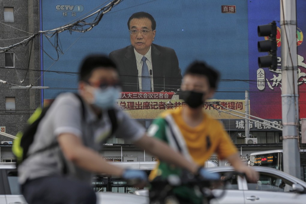 People ride their bicycles near a large screen showing a press conference by Chinese Premier Li Keqiang following the closing session of the 13th National People’s Congress in Beijing on May 28. Photo: EPA-EFE