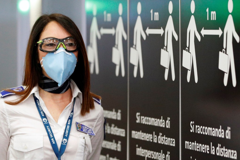 An airport security member wearing a protective face mask stands near a sign advising social distancing at Fiumicino Airport in Italy. Photo: Reuters