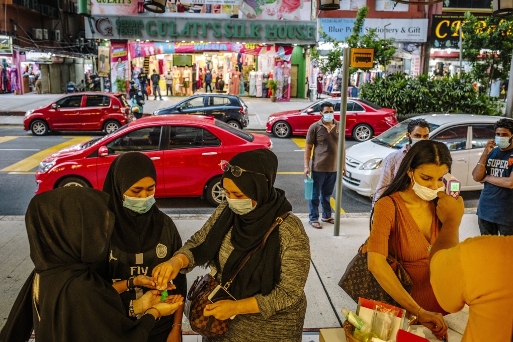 Shoppers use hand sanitiser as a stallholder checks a customer’s temperature outside a store during a partial lockdown in Kuala Lumpur, Malaysia, last month. Photo: Bloomberg
