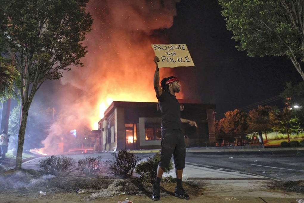 A person holds a sign as a Wendy's restaurant burns in Atlanta. Photo: AP