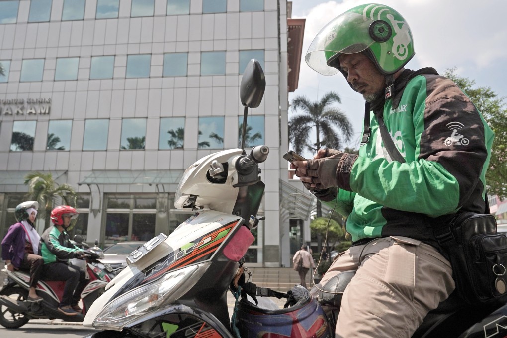 A Go-Jek motorcycle driver checks his smartphone, while preparing for another delivery in Jakarta, Indonesia. Gojek managers pledged to funnel 25 per cent of their salaries over the next year into a fund designed to support drivers, merchants and partners, following the company’s decision to cut 430 jobs. Photo: Bloomberg