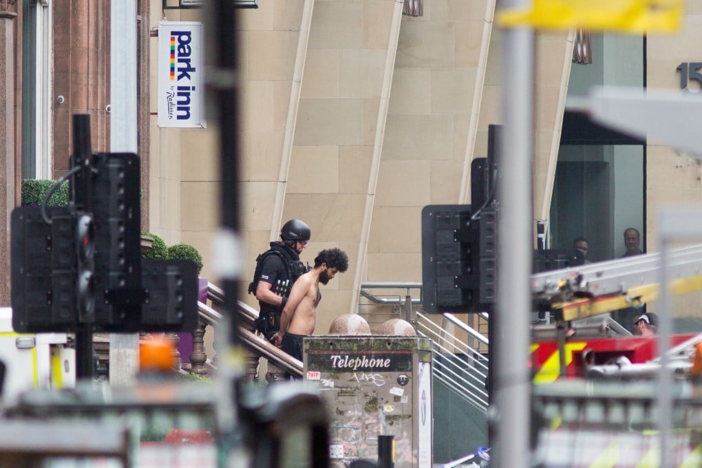 A police officer escorts a man from the Park Inn Hotel as police attend the scene of a fatal stabbing incident. Photo: AFP