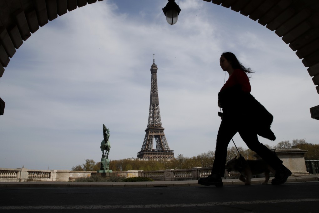 A woman walks her dog in Paris with the Eiffel tower in background. Photo: AP