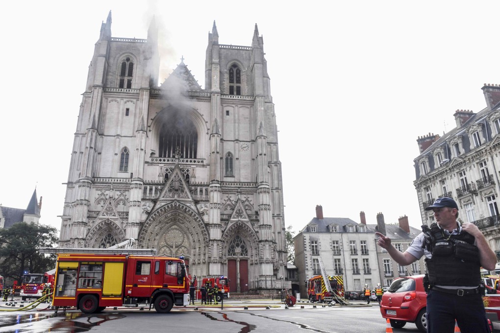 A French police officer directs traffic while firefighters work to put out a fire that broke out at Saint-Pierre-et-Saint-Paul cathedral in Nantes, causing serious damage. Photo: AFP