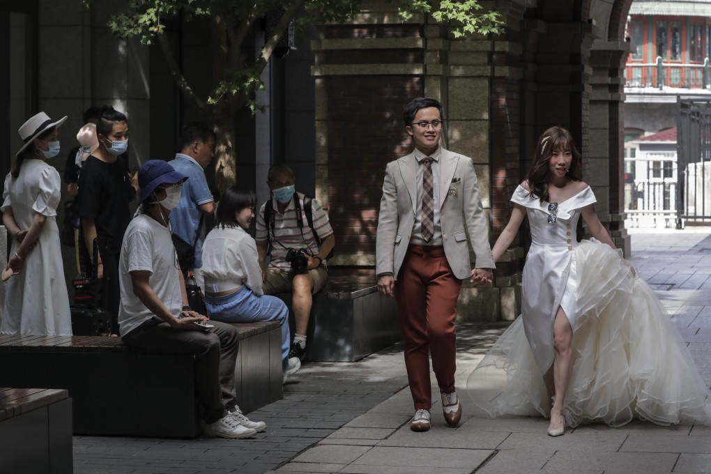 People wearing face masks watch a bride and groom pose for a pre-wedding photo shoot in Beijing on Sunday. The city’s officials will slowly unwind some Covid-19 restrictions after an outbreak was brought under control. Photo: AP