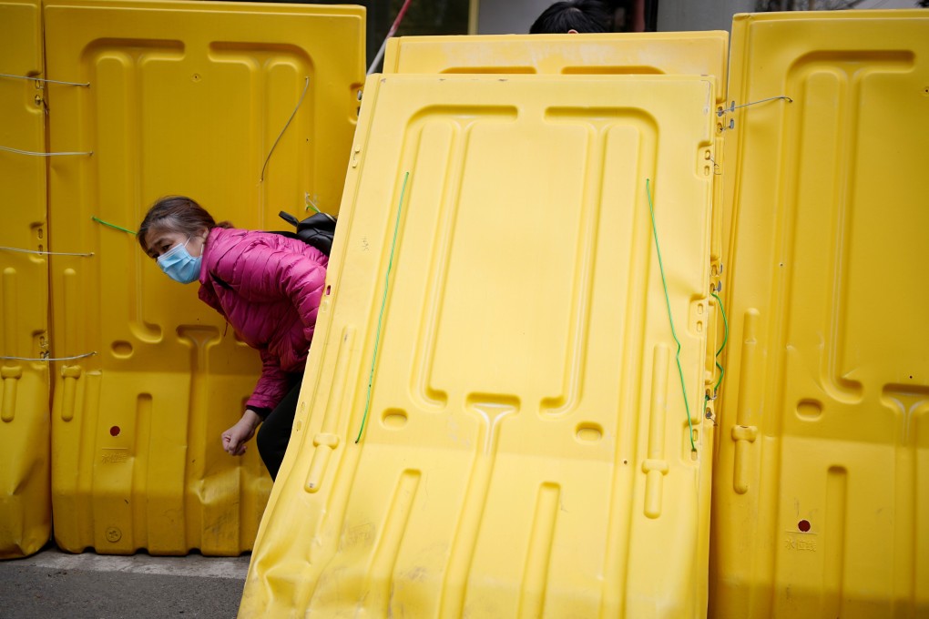 A woman wearing a face mask escapes through barriers encircling her building in Wuhan during the city’s coronavirus lockdown in April. Photo: Reuters