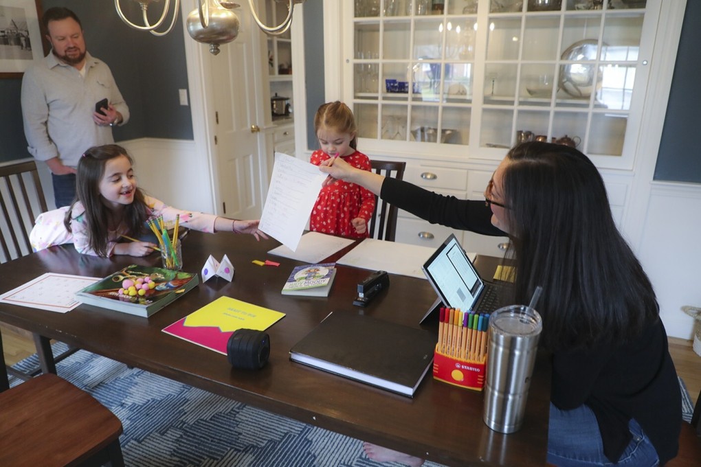 Sarah Yunits checks her daughter Ada’s homework while Cora waits her turn and father Conor Yunits takes a work call at their home in Brockton, Massachusetts, on March 19. Working from home has been a boon to many during the pandemic but has also posed personal and professional challenges during the transition. Photo: Getty Images