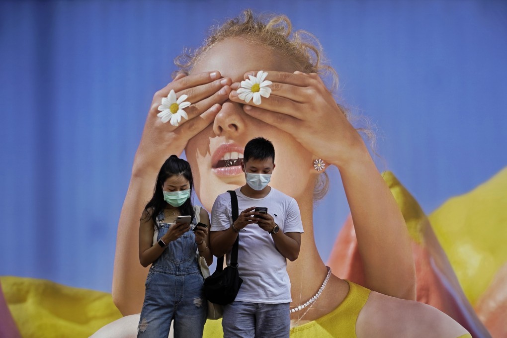 Two people wearing face masks look at their mobile phones in front of a poster in Hong Kong on Monday. The city has ordered the mandatory wearing of masks in public. Photo: AP