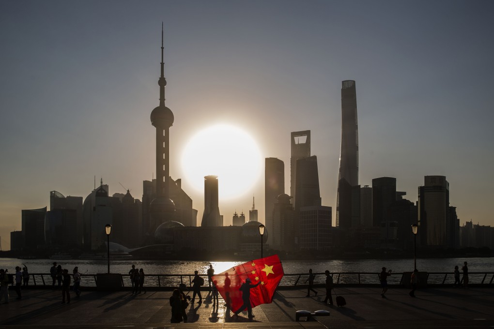 A man carrying a kite in the shape of the Chinese national flag walks along the Bund as the sun rises behind the buildings of Pudong’s Lujiazui financial district in Shanghai in October 2015. China is seeking to build heavyweight investment banks to take on foreign players. Photographer: Bloomberg