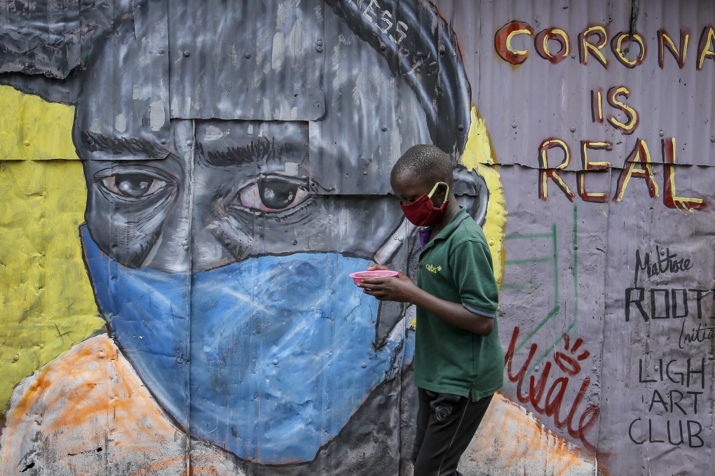 A boy wearing a face mask carries a small bowl of githeri, or mixed beans and maize, as he walks past an informational mural warning people about the risk of the new coronavirus, painted by graffiti artists from the Mathare Roots youth group, in the Mathare slum, or informal settlement, of Nairobi, Kenya Saturday, in April 2020. Photo: AP