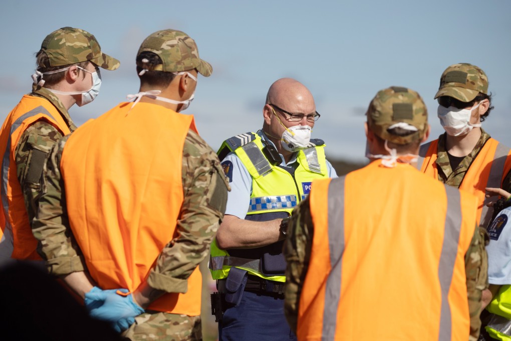 A police officer wearing a protective masks talks to defence force staff at a checkpoint in Auckland. Photo: Bloomberg