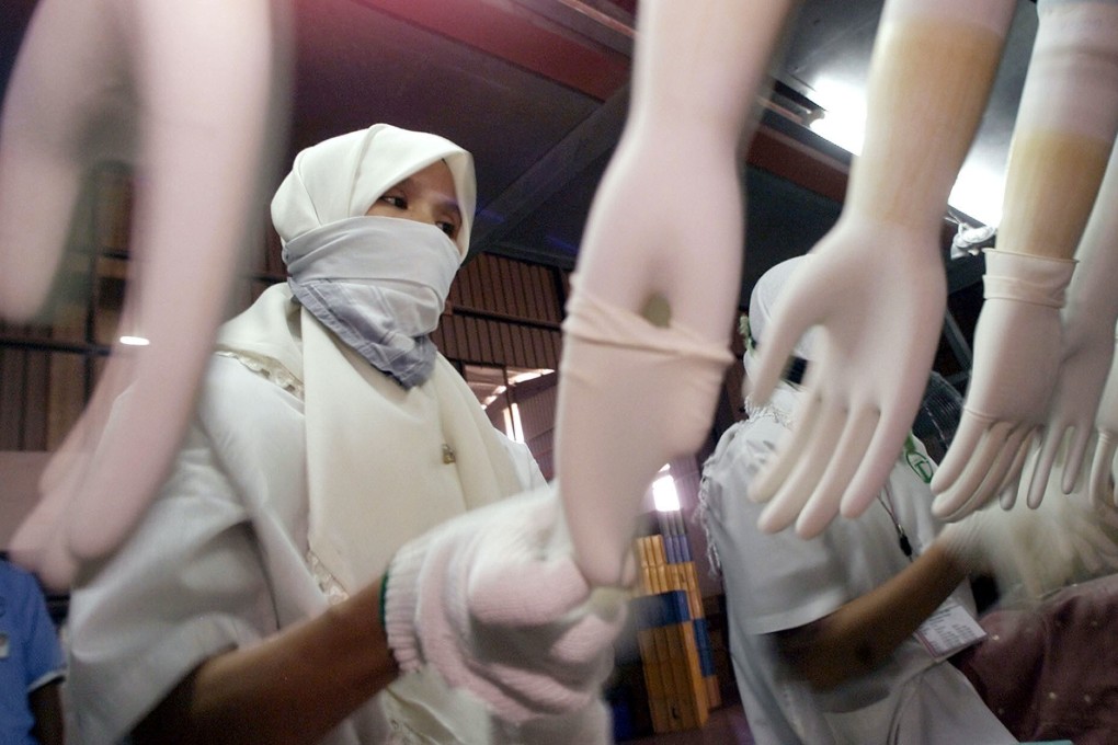 A worker removes a latex glove from a hand-shaped model on a production line. Malaysia produces about 65 per cent of the world’s supply for rubber gloves. Photo: AP