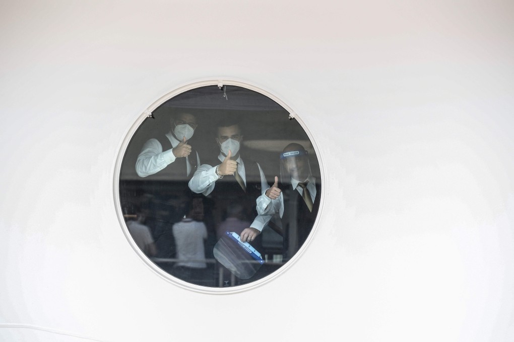 Staff members of the MSC Grandiosa cruise liner signal through a porthole before the departure of the liner from Genoa. Photo: Miguel Medina/AFP