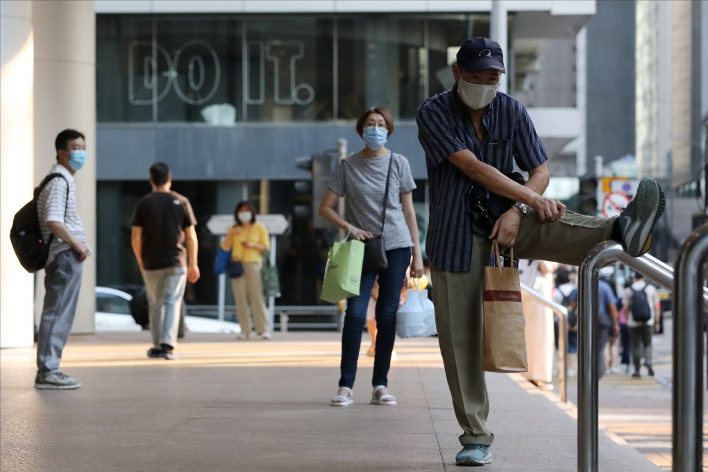 An elderly man in a face mask stretches on a handrail in Central, Hong Kong. Photo: May Tse