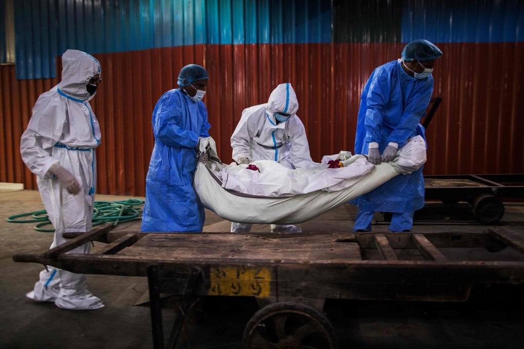 Relatives (in white) along with workers (in blue) wearing PPE help to place the body of a person who died from coronavirus in New Delhi. Photo: AFP