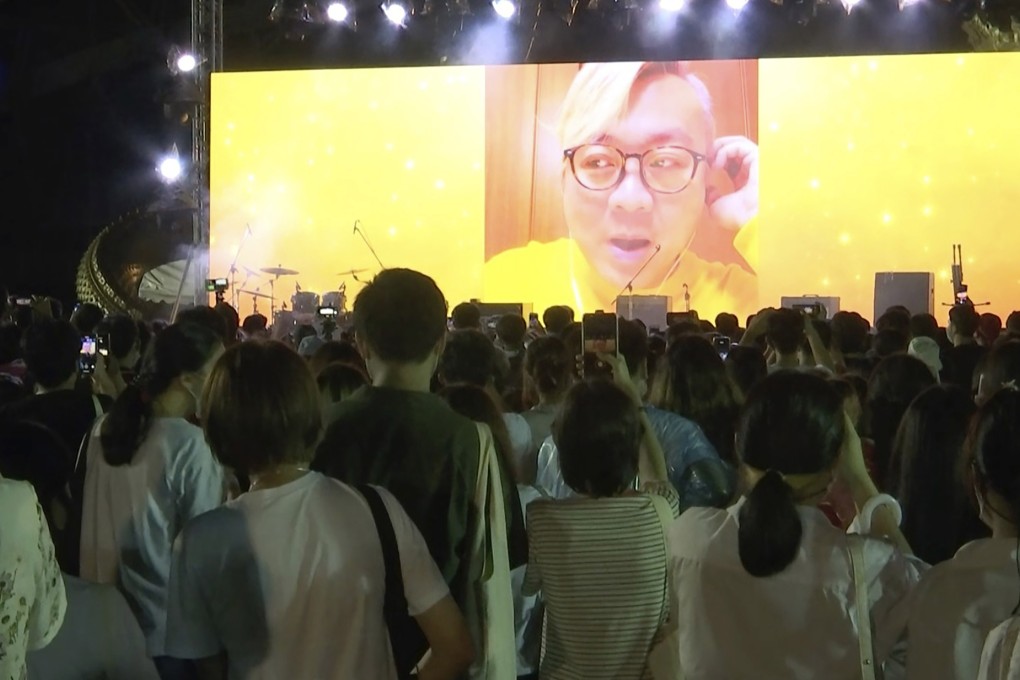 Pavin Chachavalpongpun, administrator of the Facebook group ‘Royalist Marketplace’, is shown delivering a pre-recorded message on-screen before a crowd at an anti-government rally. Photo: AP Photo