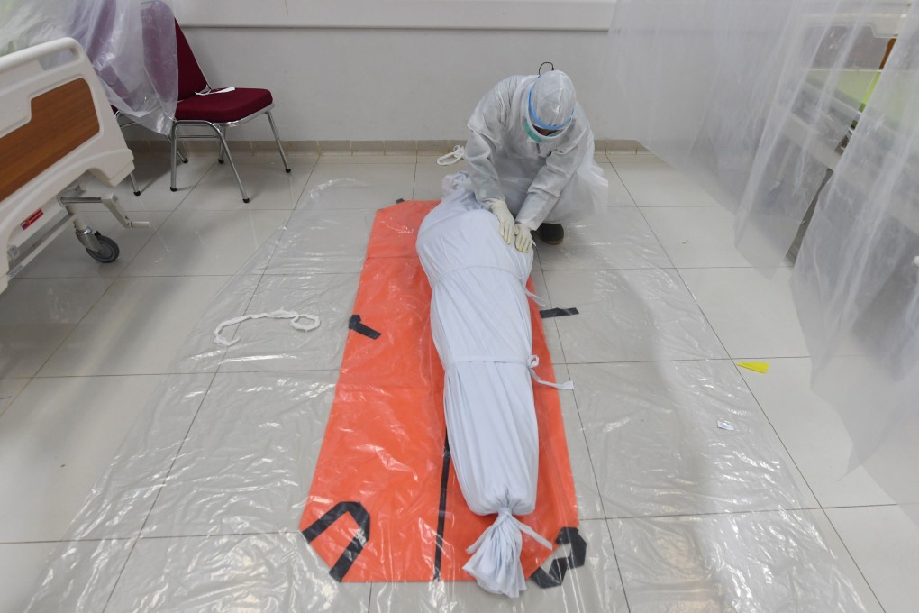 A hospital worker in Bogor, Indonesia, secures a white burial shroud over the body of a patient who died from Covid-19. Photo: AFP