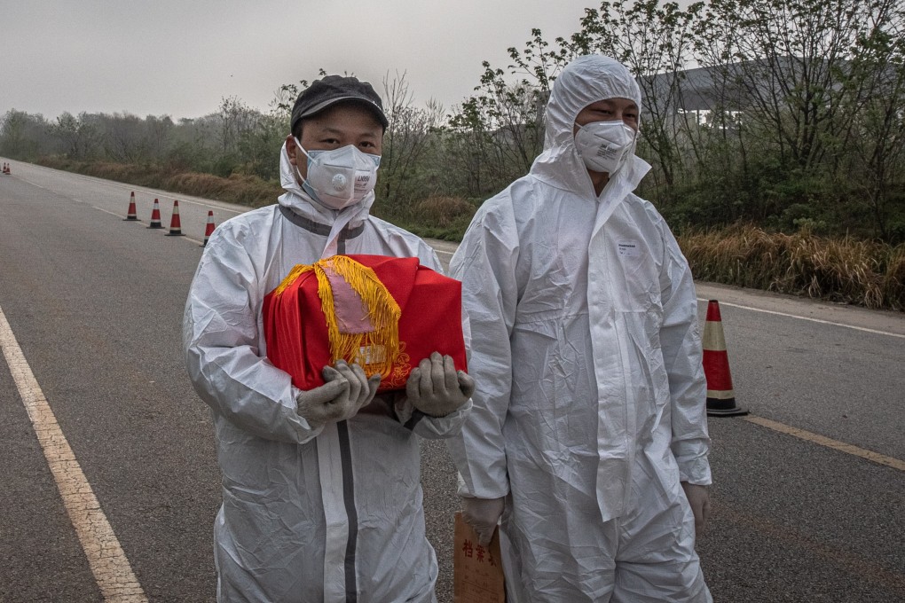 A man in full protective gear carries a box containing the ashes of a deceased person at a Wuhan funeral home during the lockdown. Photo: EPA-EFE