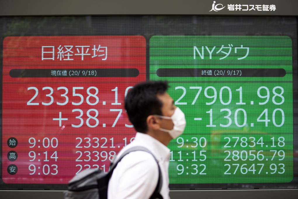 A man walks by screens showing Japan's Nikkei 225 index and the Dow Jones Industrial Average at a securities firm in Tokyo on September 18. Photo: AP