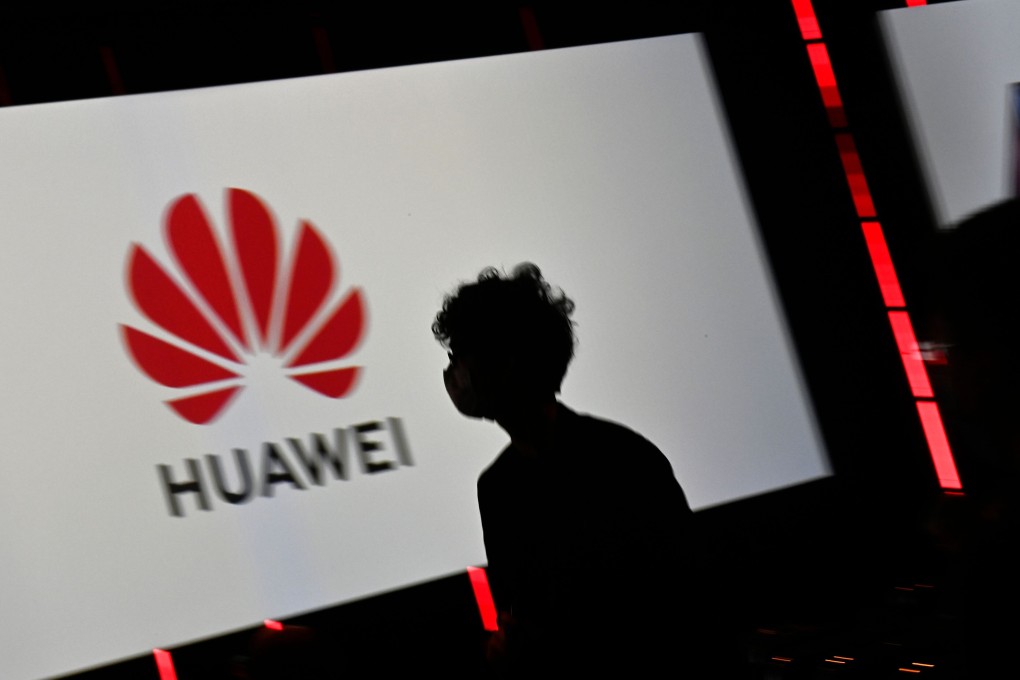 A visitor with a face mask walks past the logo of Huawei. Photo: AFP