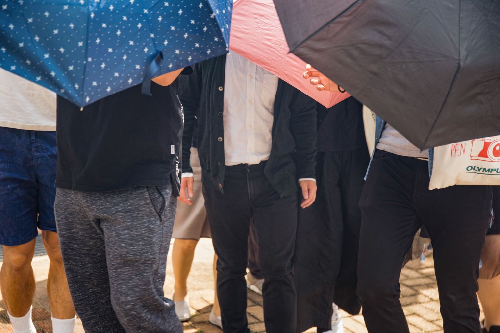 Marketing assistant Wong Chun-tik (centre) is shielded by umbrellas as he exits Fanling Court on Thursday. Photo: Brian Wong
