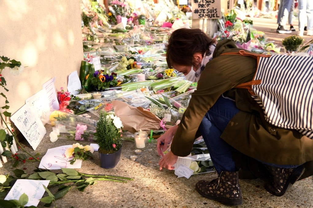 A woman lays flowers at the entrance of a school in Conflans-Sainte-Honorine, northwest of Paris, after a teacher was decapitated by an attacker who was shot dead by policemen. Photo: AFP