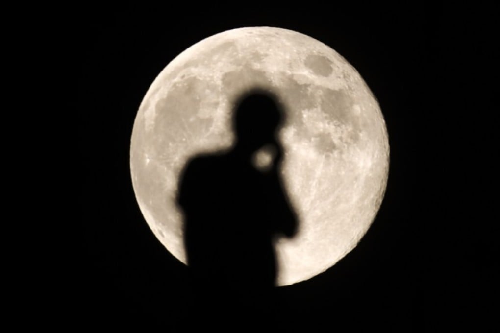 A person talking on a mobile phone is silhouetted against the full moon in Lhasa, in August 2012. Photo: Xinhua
