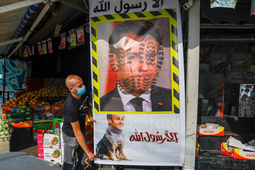 A Palestinian in East Jerusalam erects a mural with the slogan “Anyone but the Prophet” and the portrait of French President Emmanuel Macron with boot prints and placed on the body of a dog. Photo: AFP