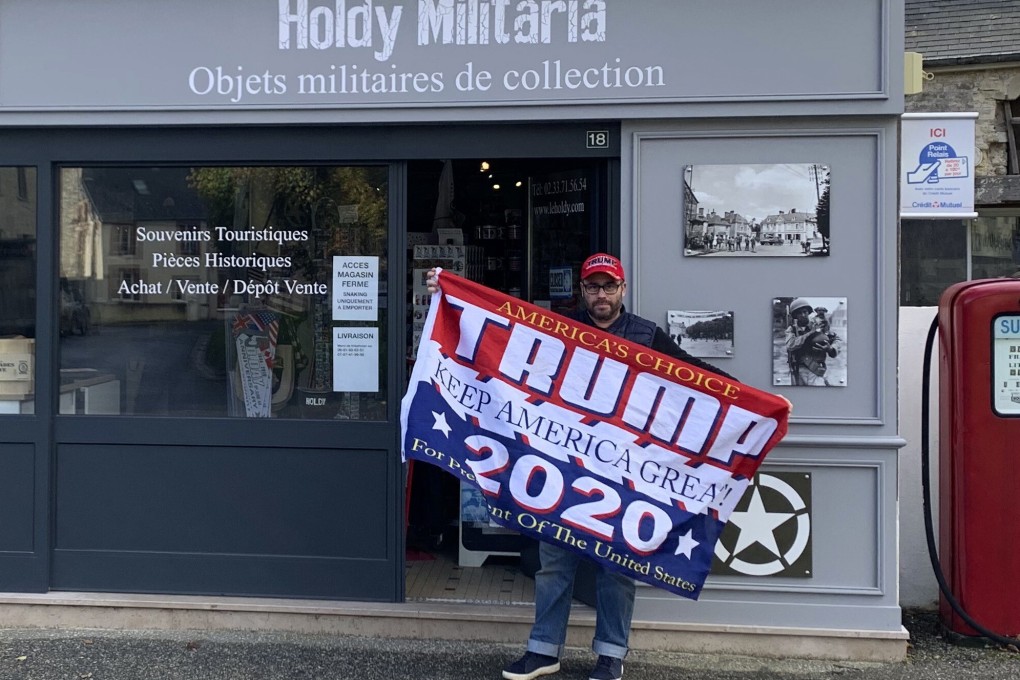 Philippe Tanne, of France, holds a Trump 2020 flag outside the military memorabilia store he runs in the Normandy town of Sainte-Marie-du-Mont on Tuesday. Photo: Philippe Tanne via AP