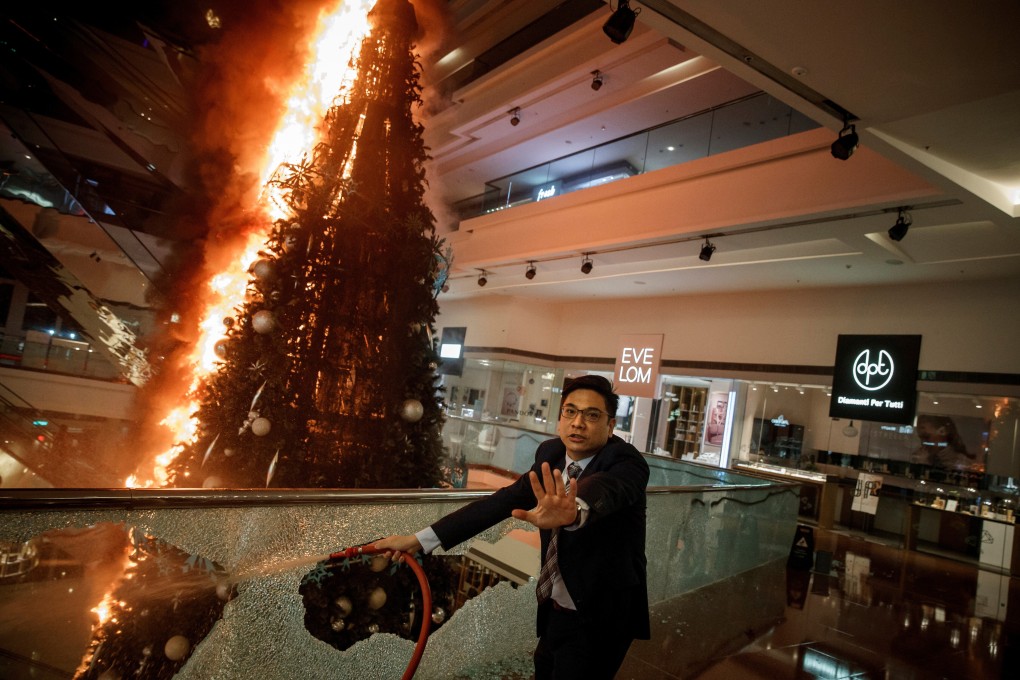 A member of security staff urges caution as he tries to extinguish a burning Christmas tree at an upscale mall in Kowloon Tong district of Hong Kong, after it was stormed by anti-government protesters on November 12, 2019. Photo: Reuters
