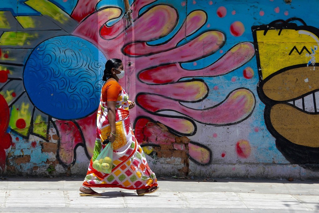 A woman wearing a mask walks by graffiti art on a roadside wall in Bangalore India on May 15. India’s entire US$7 billion vaccine budget would buy enough Pfizer doses for less than a sixth of its population. Photo: EPA-EFE