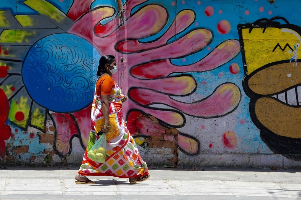 A woman wearing a mask walks by graffiti art on a roadside wall in Bangalore India on May 15. India’s entire US$7 billion vaccine budget would buy enough Pfizer doses for less than a sixth of its population. Photo: EPA-EFE