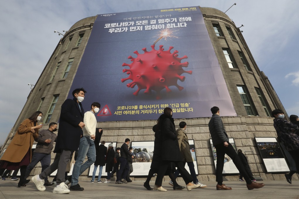 People wearing face masks walk under a banner emphasising an enhanced social distancing campaign in front of Seoul City Hall, South Korea. Photo: AP
