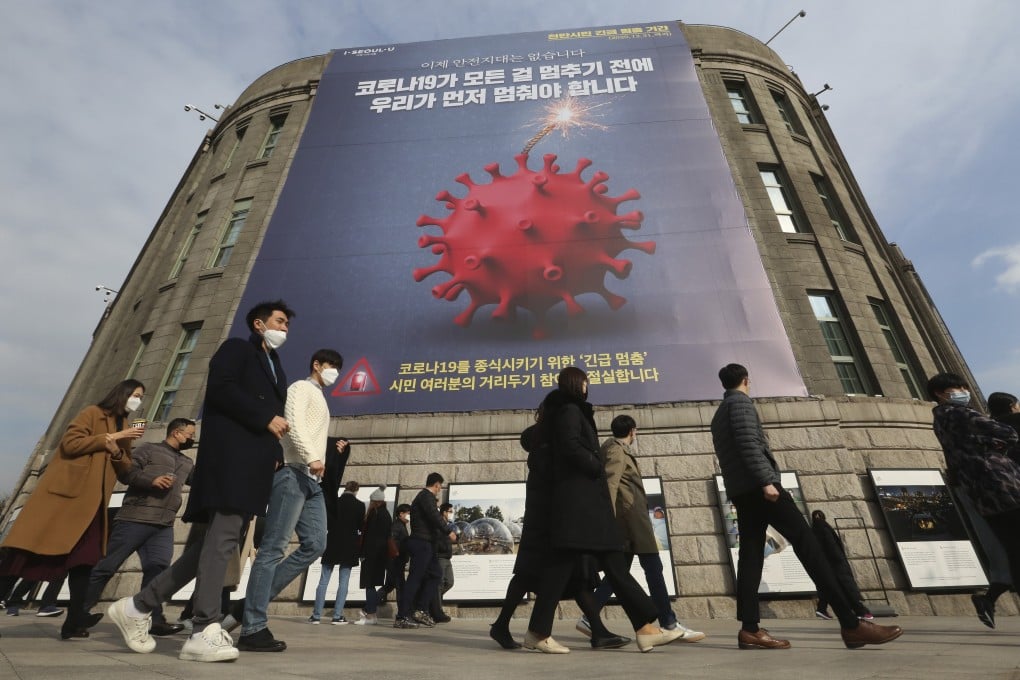 People wearing face masks walk under a banner emphasising an enhanced social distancing campaign in front of Seoul City Hall, South Korea. Photo: AP