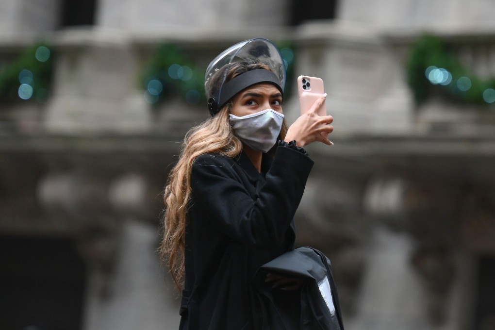 A woman takes pictures with her phone outside the New York Stock Exchange in New York City on November 30. The launch of mass vaccinations have become crucial to the outlook for the global economy and markets. Photo: AFP